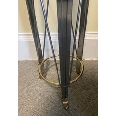 a tall black and gold metal table with glass top on carpeted floor next to wall