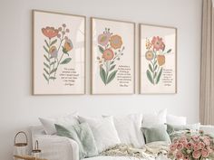 three floral prints hang on the wall above a white couch with pillows and flowers in vases