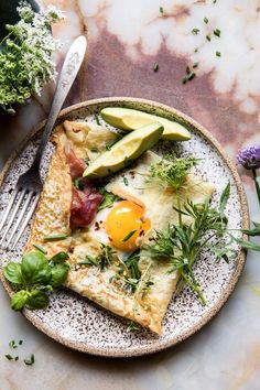 an egg and avocado pizza on a plate with a fork next to it