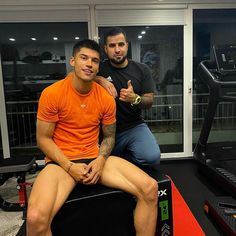 two men sitting next to each other in front of a treadmill and giving the thumbs up