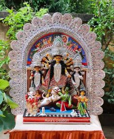 a statue of the hindu god and goddess in front of some plants on a table