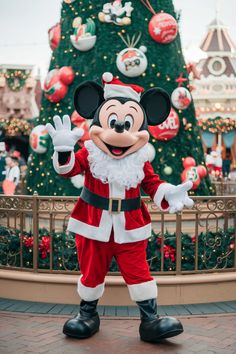 a mickey mouse dressed as santa clause in front of a christmas tree at disney world