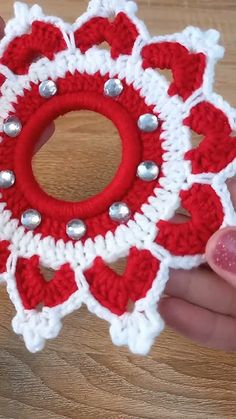 someone is holding a crocheted ornament with red and white designs on it