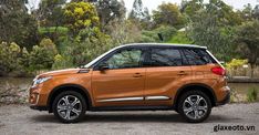 an orange car parked in front of some trees and water on the side of a road