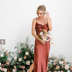 a woman standing in front of flowers wearing a red dress and holding a flower bouquet