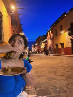 a woman sitting on the ground eating food from a plate in front of her face