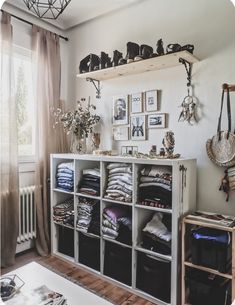 a white shelf filled with lots of clothes next to a window