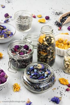 several jars filled with different types of flowers and herbs next to spoons on a table