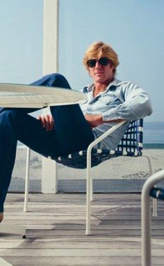 a man sitting in a chair on top of a wooden deck next to the ocean