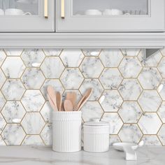 a kitchen counter with white marble and wooden utensils in front of the backsplash