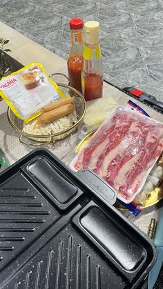 an outdoor grill with meat and condiments sitting on the table next to it