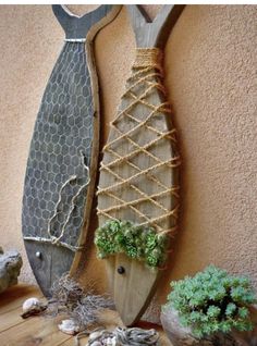 two fish shaped sculptures are on display next to plants and rocks in front of a stucco wall