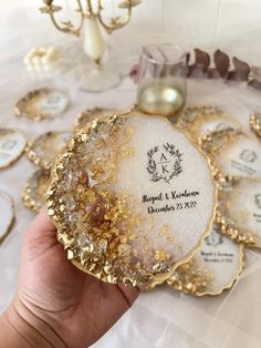 a person holding up some gold and white coasters on a table with other plates