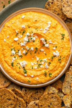 a bowl of hummus and crackers on a plate next to some pita chips