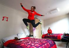 a woman jumping in the air over a bed with two other people sitting on beds behind her