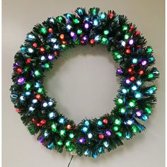 a christmas wreath with multicolored lights hanging on a wall next to a cord