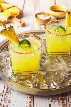 two glasses filled with drinks sitting on top of an ice covered tray next to sliced bananas