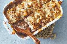 a casserole dish with meat and vegetables in it on a blue surface next to a wooden spoon