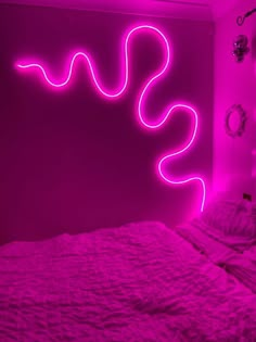 a pink neon sign in the corner of a room next to a bed with white sheets