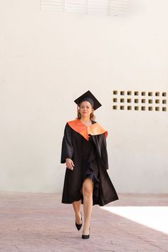 a woman in a graduation gown and cap walks down the street with her hand on her hip