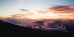 the sun is setting over some clouds on top of a mountain