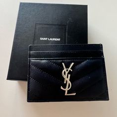 a black saint laurent card case sitting on top of a white table next to a box