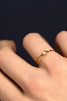 a person's hand with a gold ring on their left and a pearl bead in the middle