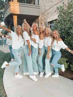 a group of women standing next to each other in front of a brick building with their arms up