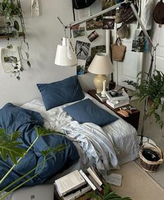 a bed with blue sheets and pillows in a room filled with potted plants on the wall