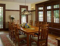 a dining room table with chairs and flowers on the table in front of large windows