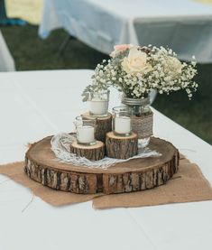 a wooden slice with candles and flowers in it on top of a white table cloth