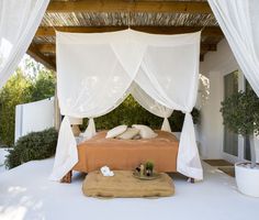 a bed sitting under a white canopy next to a lush green bush filled with flowers