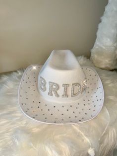 Grab this Adorable White Cowboy style Hat! Featuring BRIDE in silver and pearl decorations with the rim of the hat covered in scattered crystals. This Western style novelty hat is so fun! It is perfect for Night or a Bachelorette Party! Sized approximately 62 cm, it's great for both Men and Women! Wear it on your Wedding Day! Stylish and bedazzling, this Country Style hat is great for Rodeo style weddings, bridal shower supplies, and more!  The cute hat is lightweight and made of soft polyester. Spot clean only. White Bride Cowboy Hat, Silver Wide Brim Costume Hat With Adjustable Fit, White Hats With Rhinestones And Curved Brim, Silver Wide Brim Adjustable Costume Hat, White Rhinestone Hat With Curved Brim, Silver Adjustable Wide Brim Costume Hat, Silver Hat With Rhinestones For Rodeo, Silver Rhinestone Hat For Rodeo, White Adjustable Hat With Rhinestones