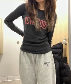 a woman standing in front of a mirror wearing sweat pants and a new york shirt