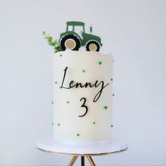 a birthday cake with a tractor on top and the number 3 in green dots is sitting on a stand