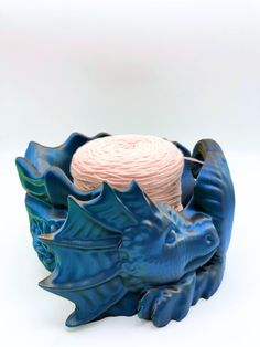 a blue ceramic bowl with a pink yarn ball in it's center and two dragon heads on the base