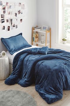 a bed with blue comforter and pillows in a bedroom next to a white wall