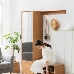 a woman sitting on top of a wooden cabinet in a living room next to a chair