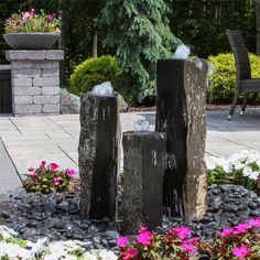 two large rocks sitting next to each other on top of a rock garden bed with flowers