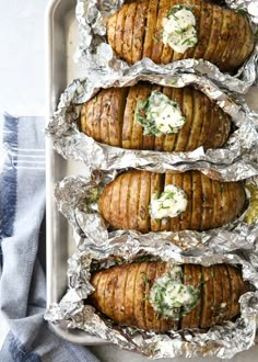 baked potatoes in foil lined up on top of each other and topped with sour cream