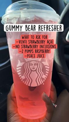 a person holding up a cup with pink liquid in it that says gummy bear refresher