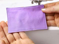 two hands are holding a purple cloth in front of a sewing machine that is stitching