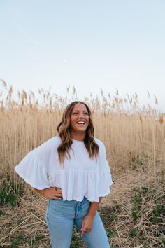 a woman standing in the middle of a field with her hands on her hips and smiling