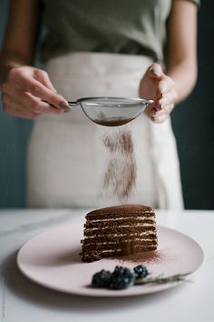 a person is sprinkling sugar on a stack of pancakes with berries and blueberries