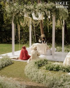 a man and woman sitting on a white bench under a canopy in the middle of a garden