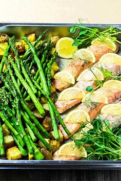 a pan filled with fish, asparagus and lemons