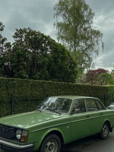 an old green car parked in front of a hedge