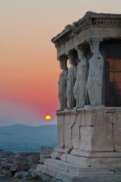 the sun is setting behind some statues on top of a building with mountains in the background