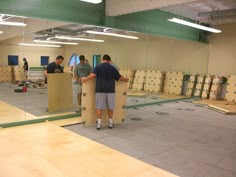 two men are standing in an empty room with boxes on the floor and one man is looking at his cell phone