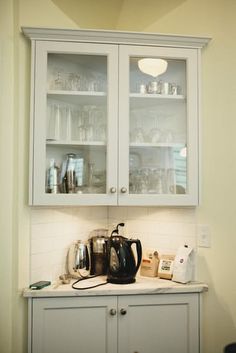 a kitchen with white cabinets and glass front cupboards filled with coffee pots, teapots and other items